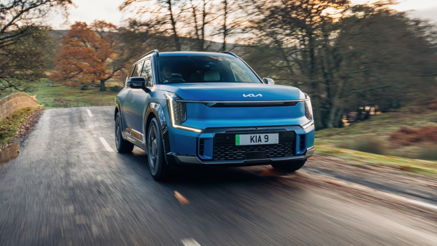 A blue EV9 GT driving through a wooded road