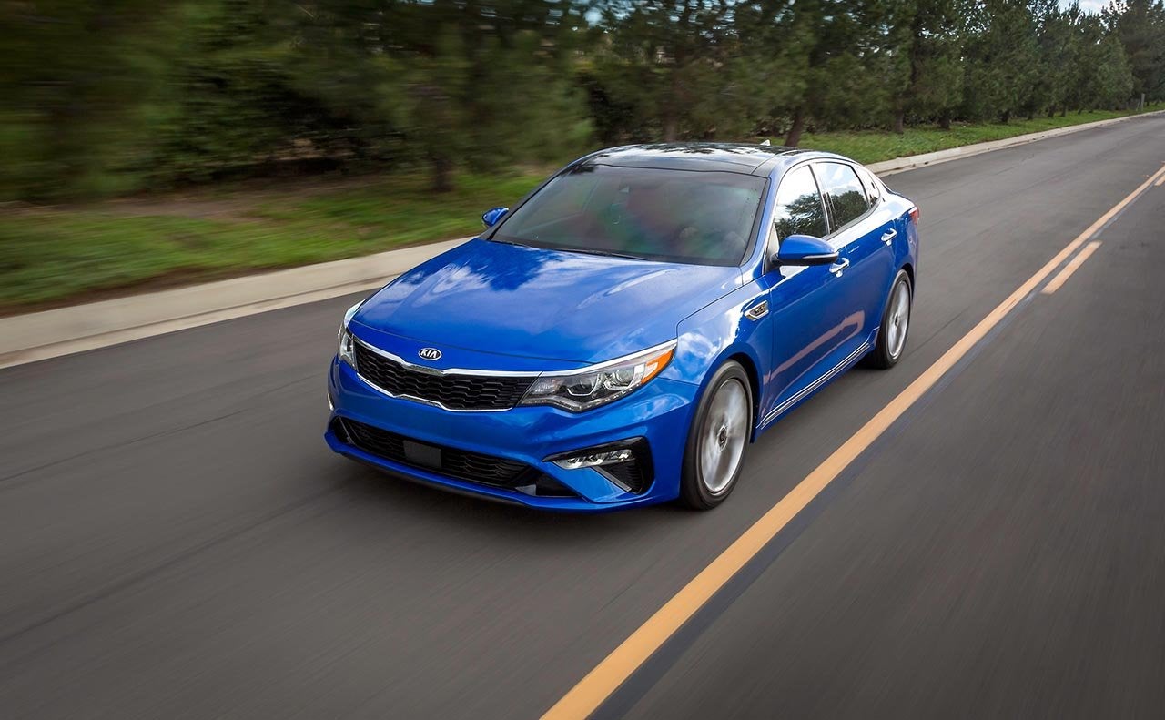Image of a blue 2019 Kia Optima driving on a country highway.